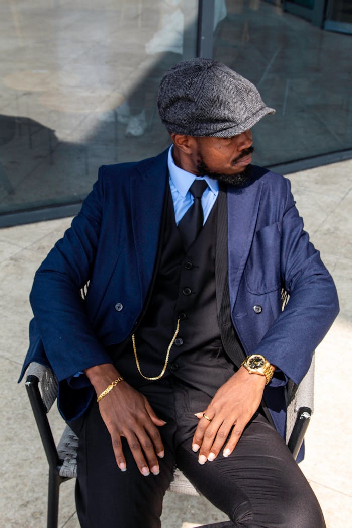 Fashionable man in vintage attire seated outdoors in bright sunlight.
