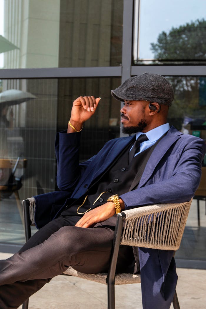Fashionable man sitting outdoors in a blue suit and cap, exuding elegance and style.
