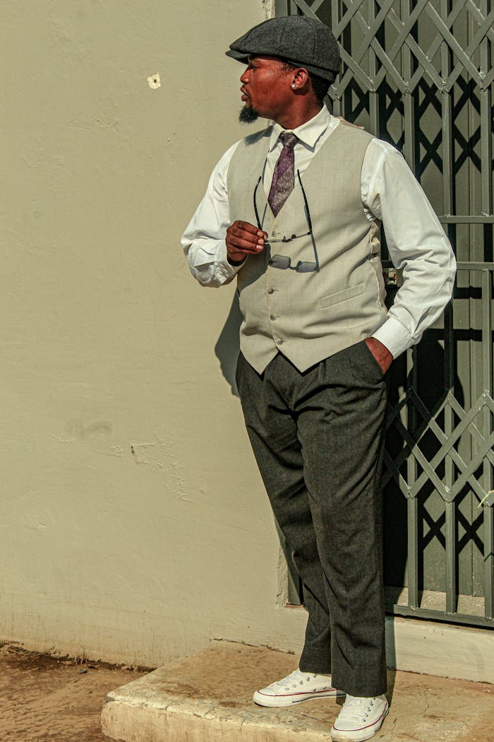 Man in classic attire posing outdoors, exuding elegance with stylish hat and vest.